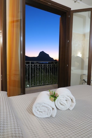 A hotel room with a bed, a balcony with a view of a mountain, and a window with curtains.
