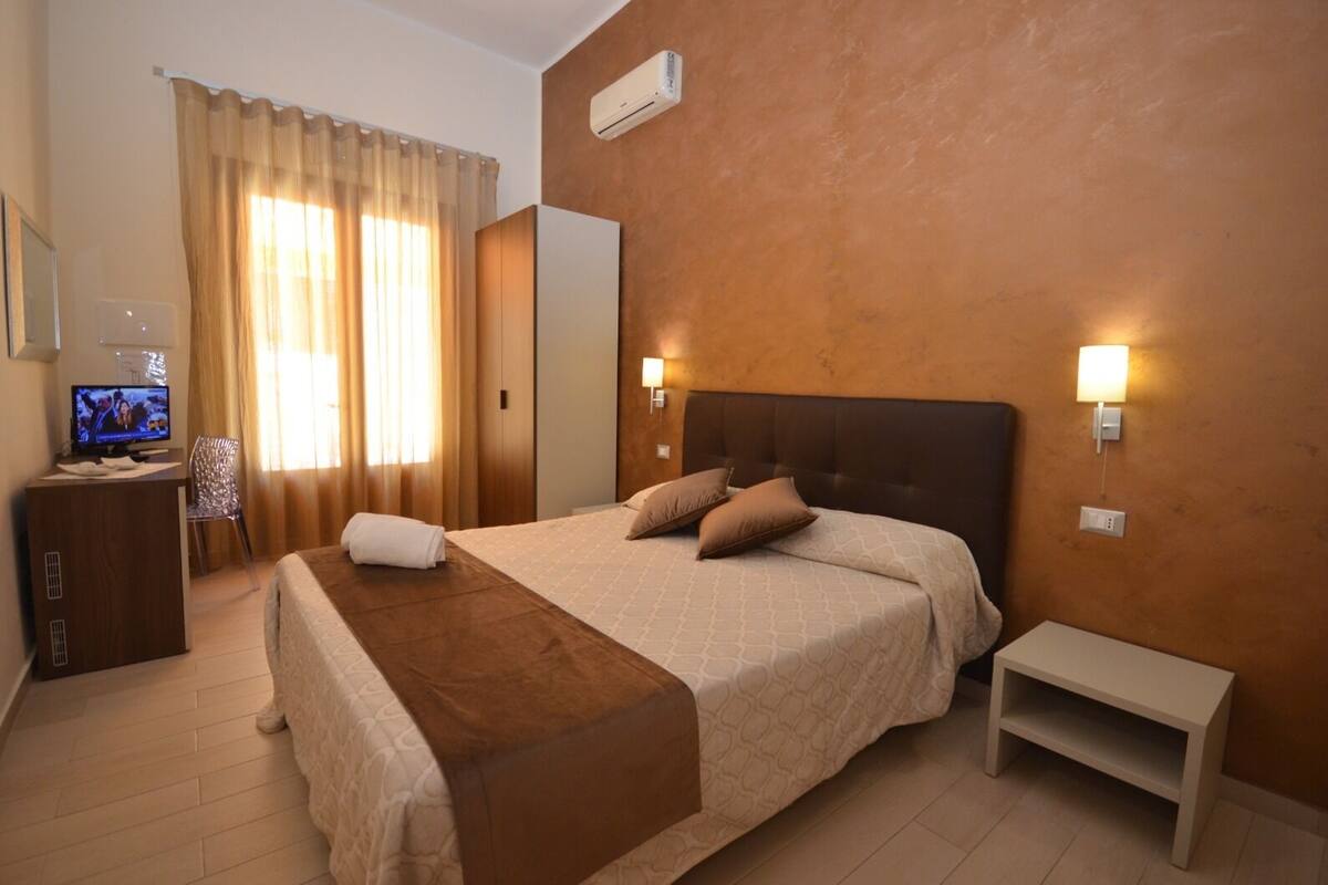 Une chambre d’hôtel avec un grand lit, un téléviseur posé sur un bureau et un climatiseur fixé au mur.