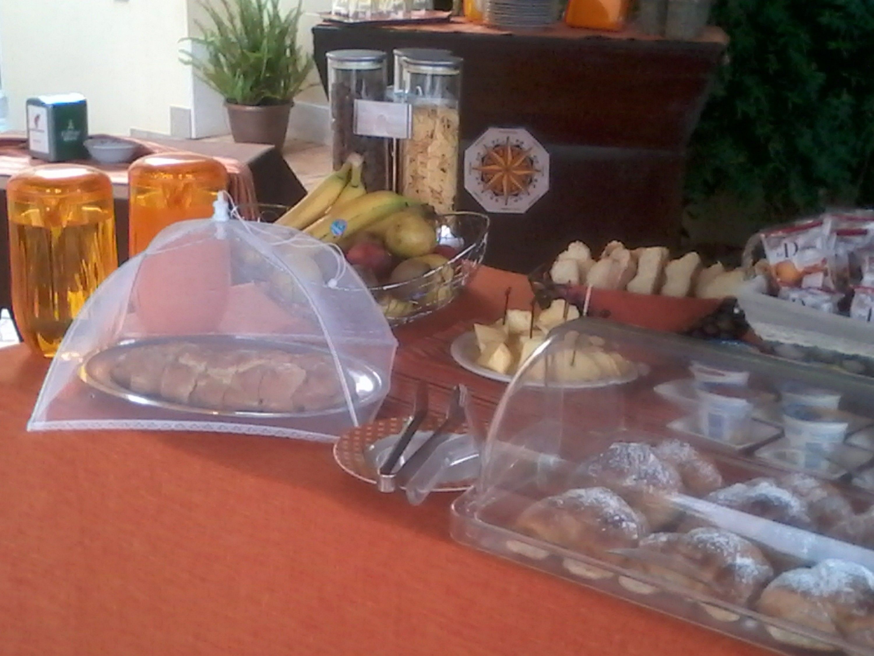 Una mesa de buffet con diversos alimentos, entre ellos frutas, pasteles y un recipiente tapado.