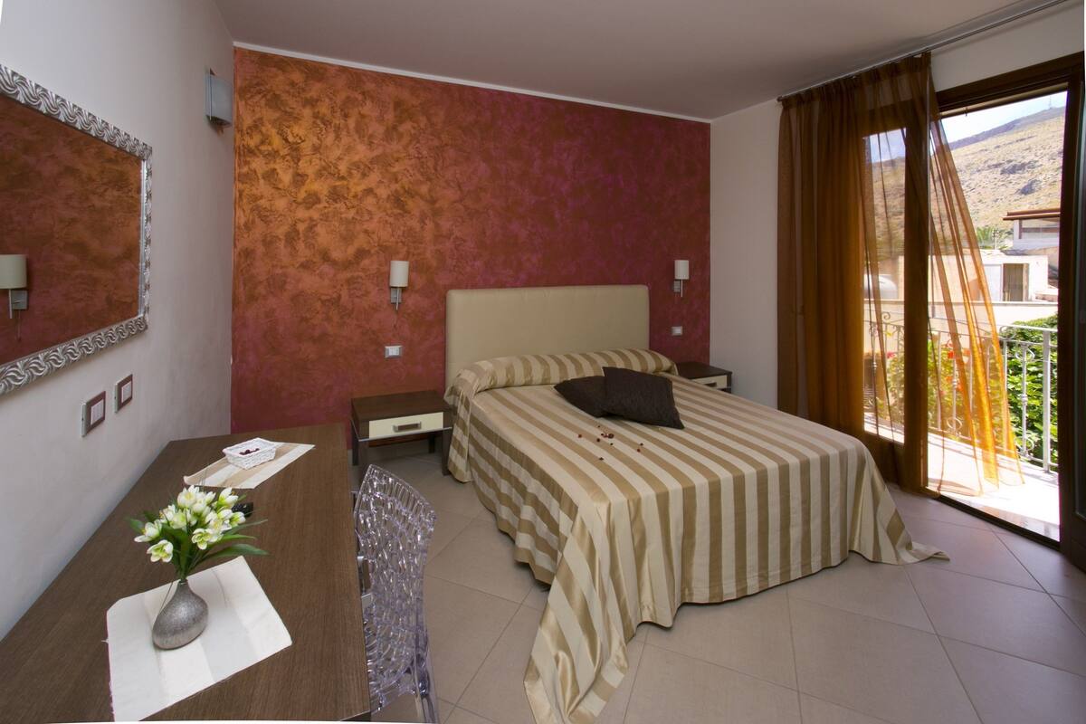 Une chambre d’hôtel avec un lit, un bureau agrémenté d’un vase de fleurs, un miroir et une vue sur l’extérieur.
