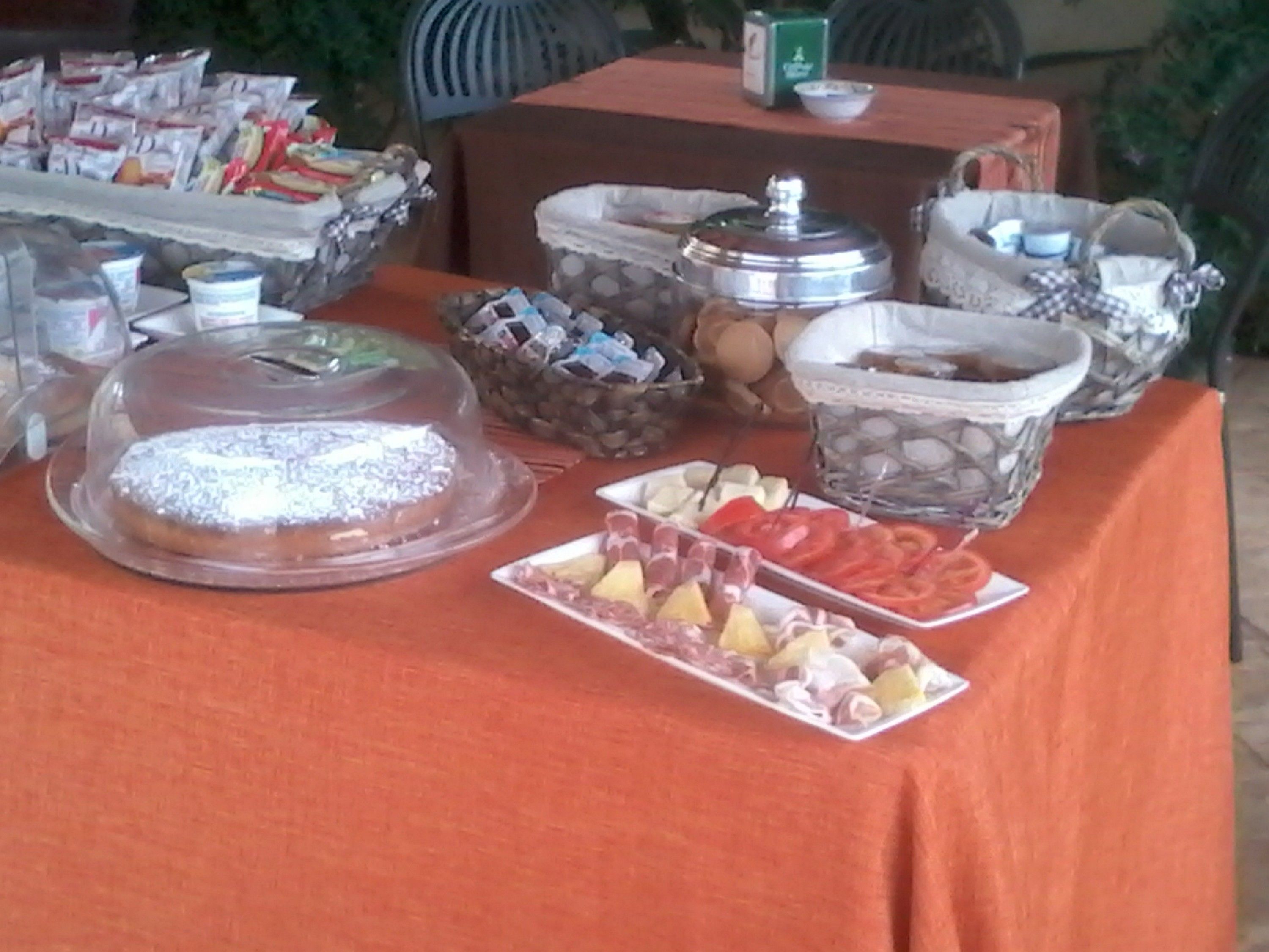 Ein reichhaltiges Buffet mit verschiedenen Speisen, darunter eine abgedeckte Torte, Obst und Behälter mit Snacks.