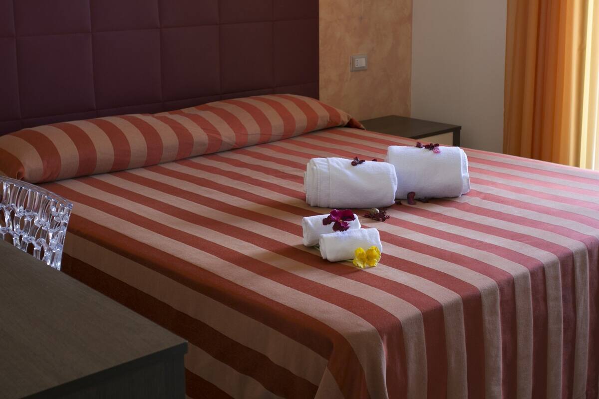 Une chambre d’hôtel avec un grand lit, une literie à rayures, une tête de lit, une table de chevet et une lampe fixée au mur.
