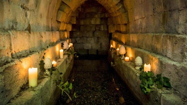 Un corredor de piedra con techos abovedados, iluminado por velas y decorado con hiedra.