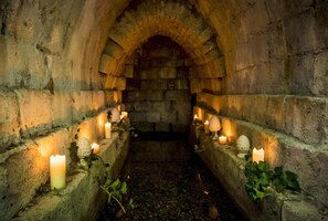 Un corredor de piedra con techos abovedados, iluminado por velas y decorado con hiedra.