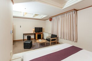 A hotel room with a bed, a desk with a television, a chair, a small table, and a window with curtains. - Noblesse Tourist Hotel (Seoul)