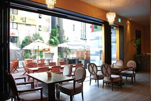 An indoor dining area with wooden tables and chairs, large windows, and a chandelier. - Noblesse Tourist Hotel (Seoul)