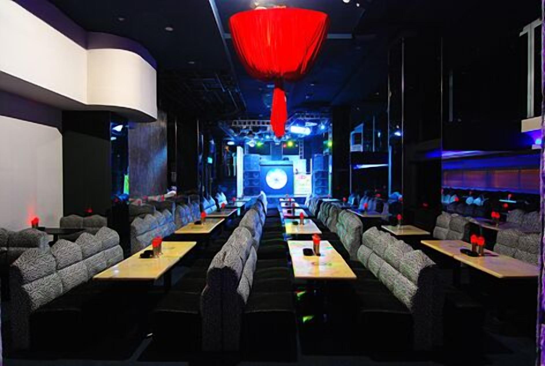 A modern restaurant with booths and tables, a red hanging light fixture, and a stage in the background.