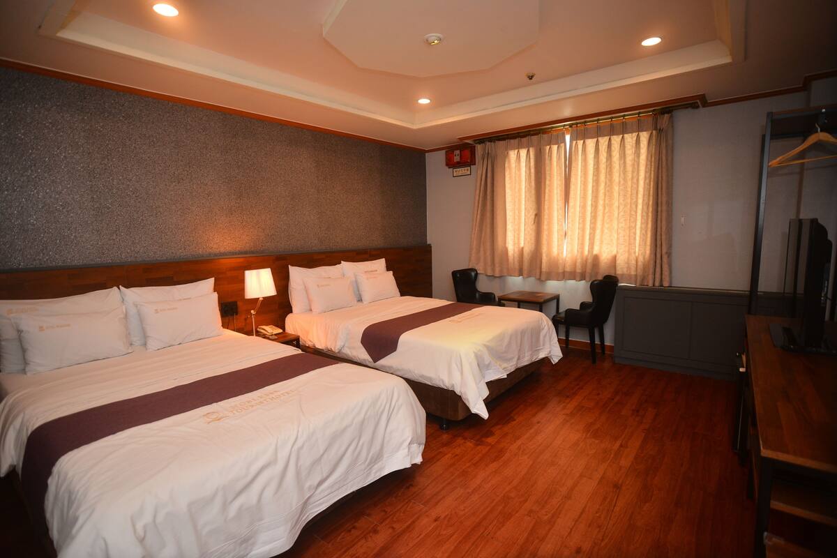 A hotel room with two beds, a desk, a chair, a small table, and a window with curtains.