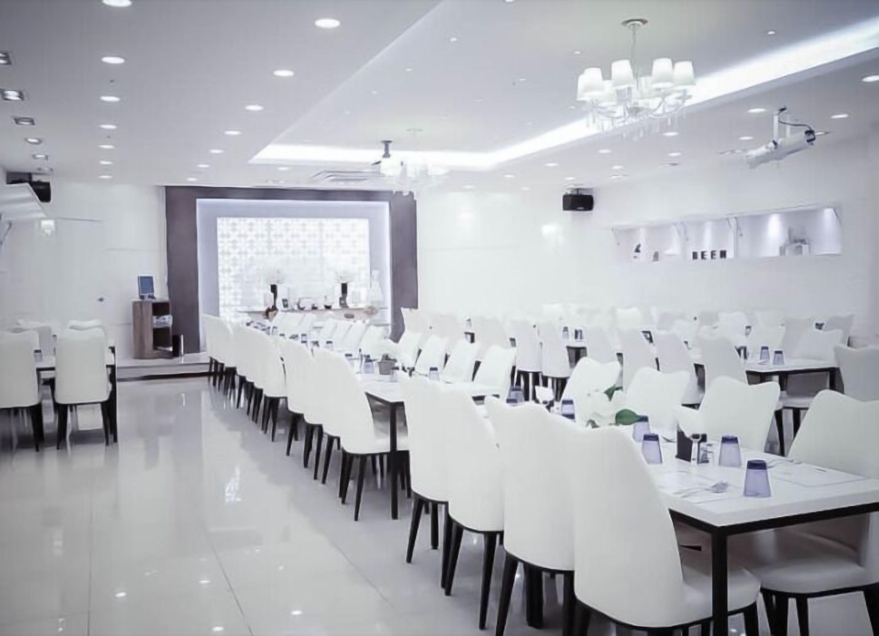 A modern conference room with white tables and chairs, a large screen, and a chandelier.