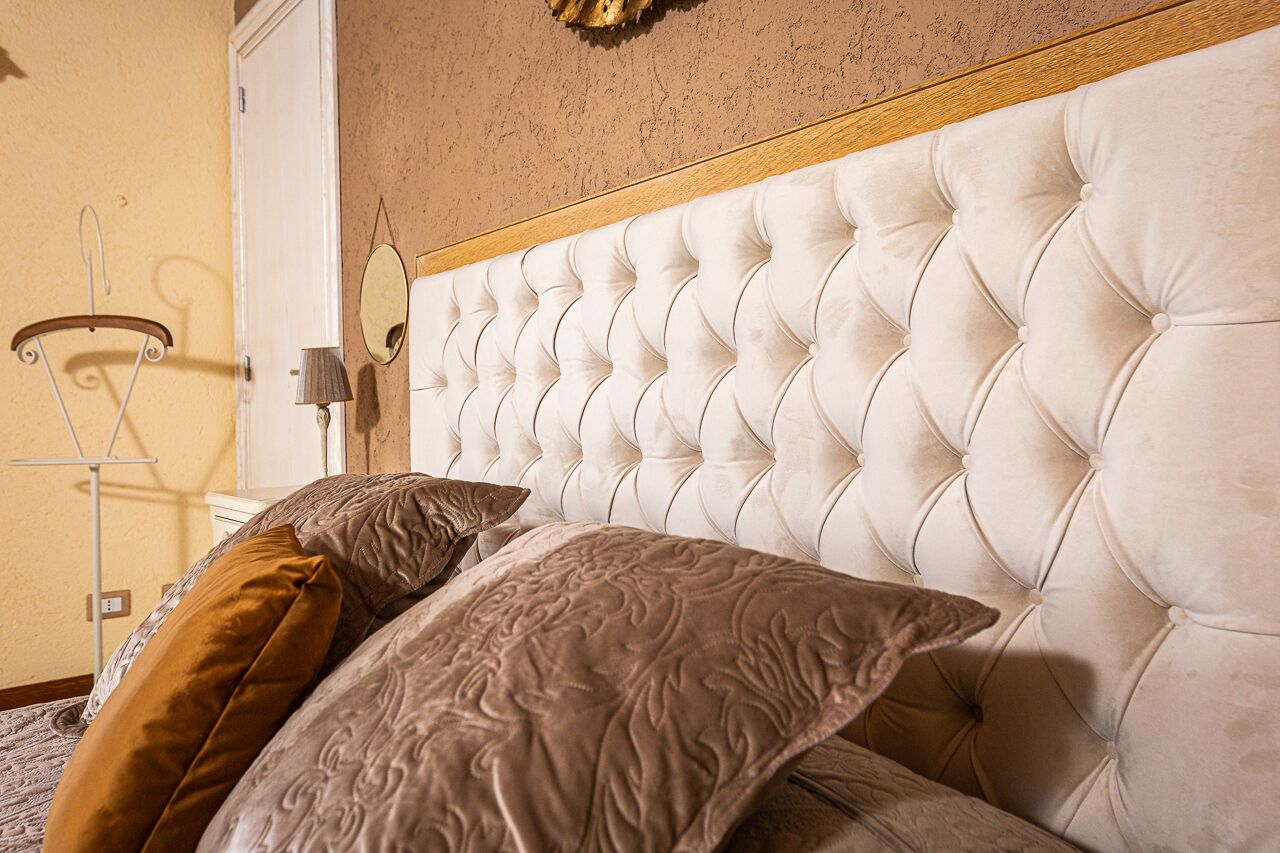 A bed with a tufted headboard, a mirror, and a lamp on a bedside table.