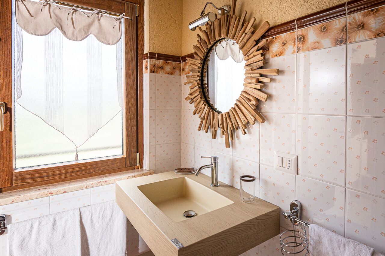 A bathroom with a wooden vanity, a sink, a mirror, and a window with a curtain.