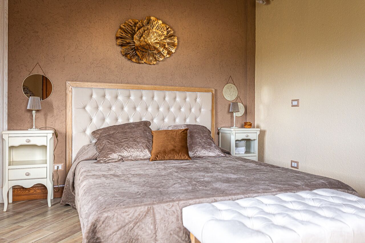 A bedroom with a tufted headboard, a large round mirror, and a decorative wall piece.