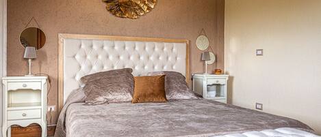 A bedroom with a tufted headboard, a large round mirror, and a decorative wall piece.