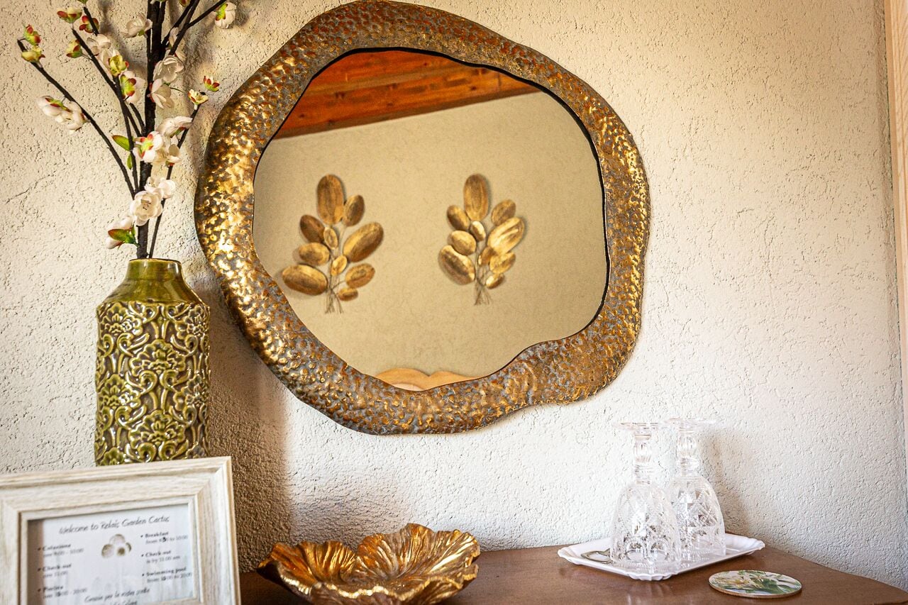 A decorative mirror with a gold frame, a vase with artificial flowers, and a framed welcome sign.