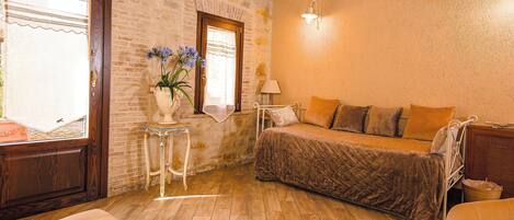 Una habitación acogedora con una cama, una mesita con un florero, una lámpara y una ventana con vistas.