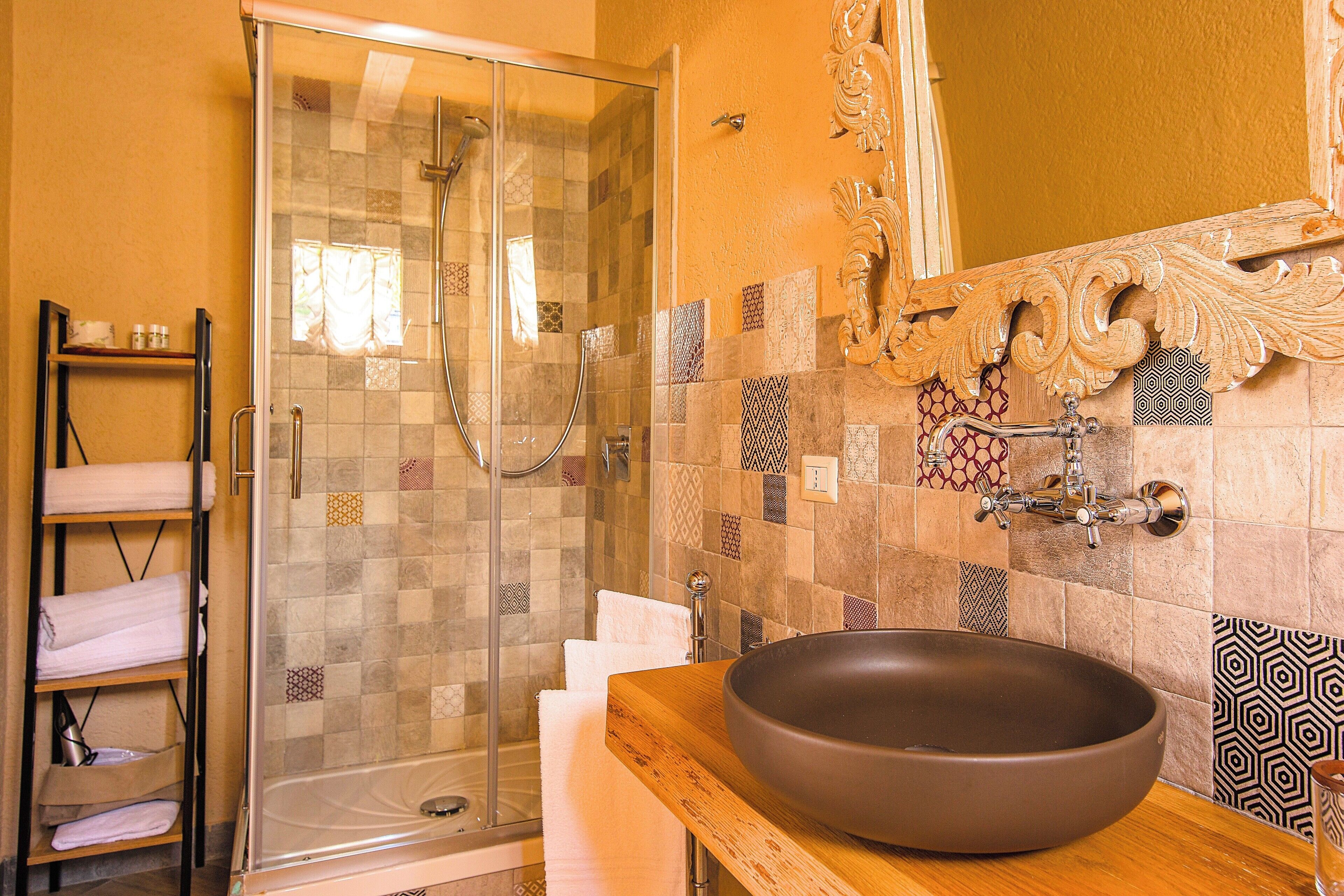 A bathroom with a glass shower enclosure, a wooden vanity with a large vessel sink, and a tiled backsplash with various patterns.