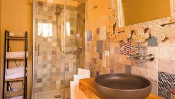 A bathroom with a glass shower enclosure, a wooden vanity with a large vessel sink, and a tiled backsplash with various patterns.