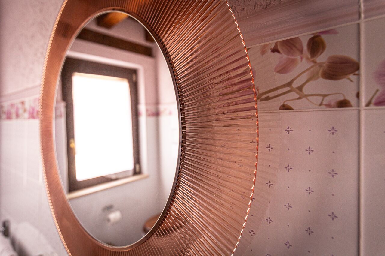 A bathroom with a round mirror, a window, and floral-patterned tiles.
