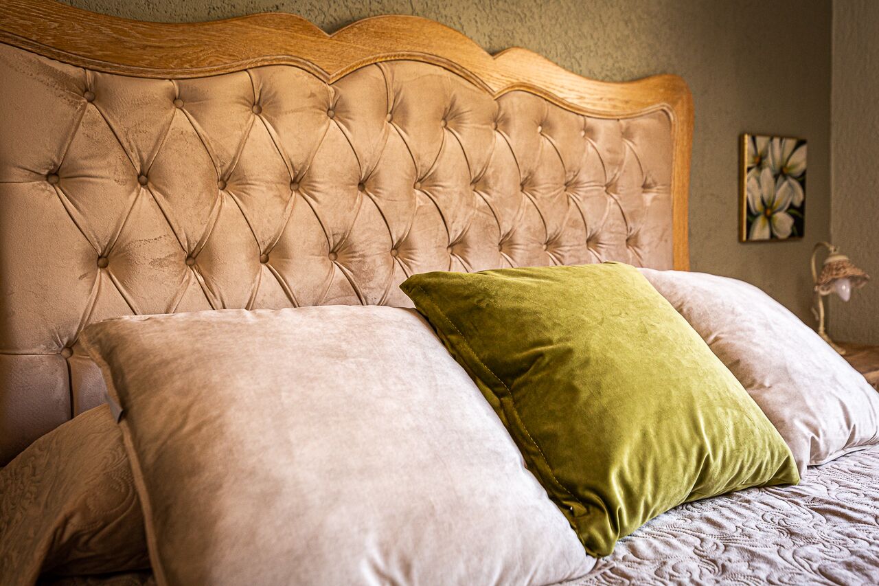 A bed with a tufted headboard, two pillows, and a wall with a floral painting.