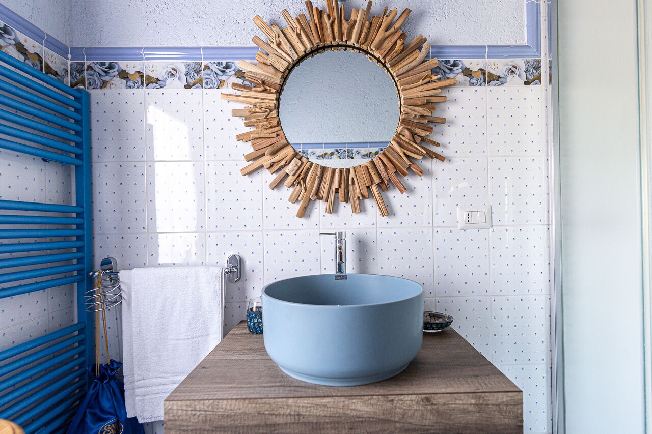 A bathroom with a blue sink, a wooden vanity, a blue towel rack, and a mirror with a sunburst frame.