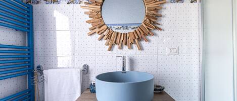 A bathroom with a blue sink, a wooden vanity, a blue towel rack, and a mirror with a sunburst frame.