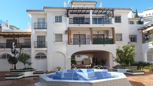 A courtyard with a central fountain, surrounded by a white building with balconies and a tiled floor. - Pueblo Quinta (Benalmádena)