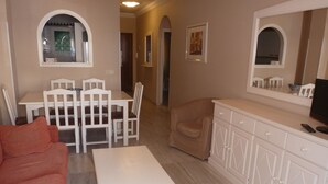 A living room with a sofa, a dining table with chairs, a small armchair, and a TV on a cabinet. - Pueblo Quinta (Benalmádena)