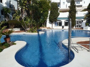 A swimming pool surrounded by lush greenery and a white building with balconies.