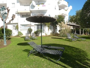 A courtyard with lounge chairs and thatched umbrellas, surrounded by white buildings with balconies.