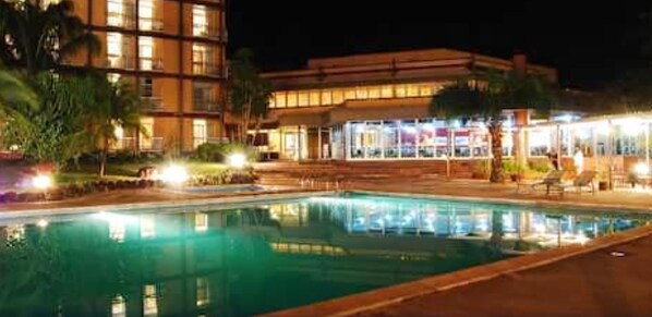 A nighttime view of a hotel with a swimming pool, outdoor seating, and a well-lit building facade. - Nike Lake Resort (Enugu)