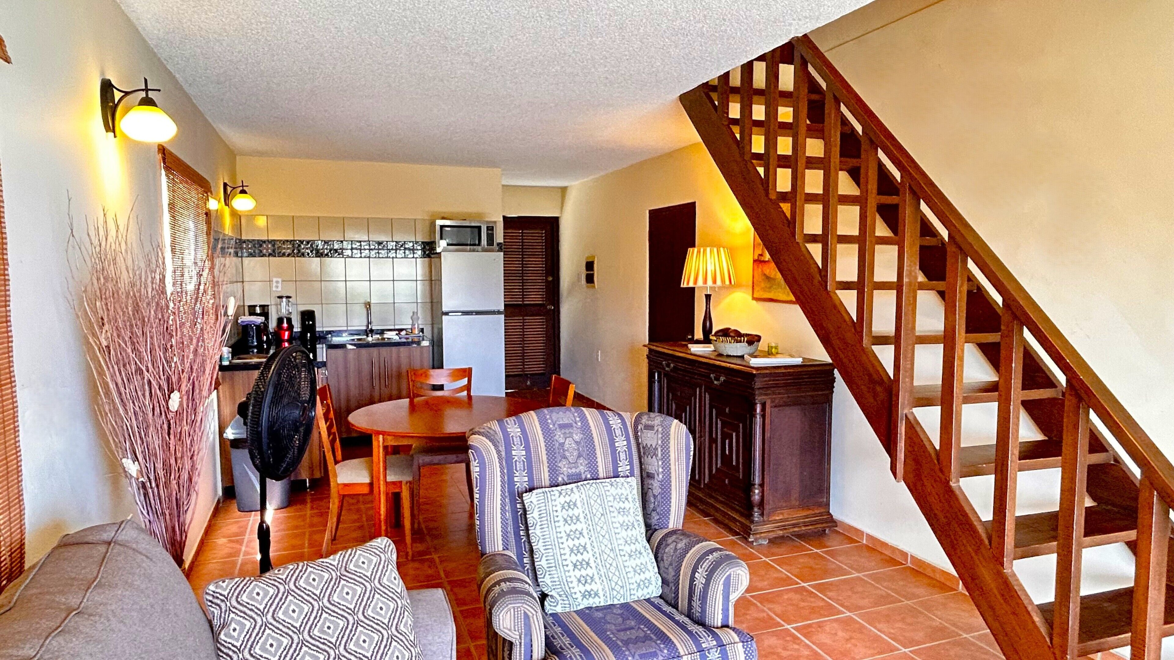 A living room with a sofa, two armchairs, a dining table, and a kitchen in the background.