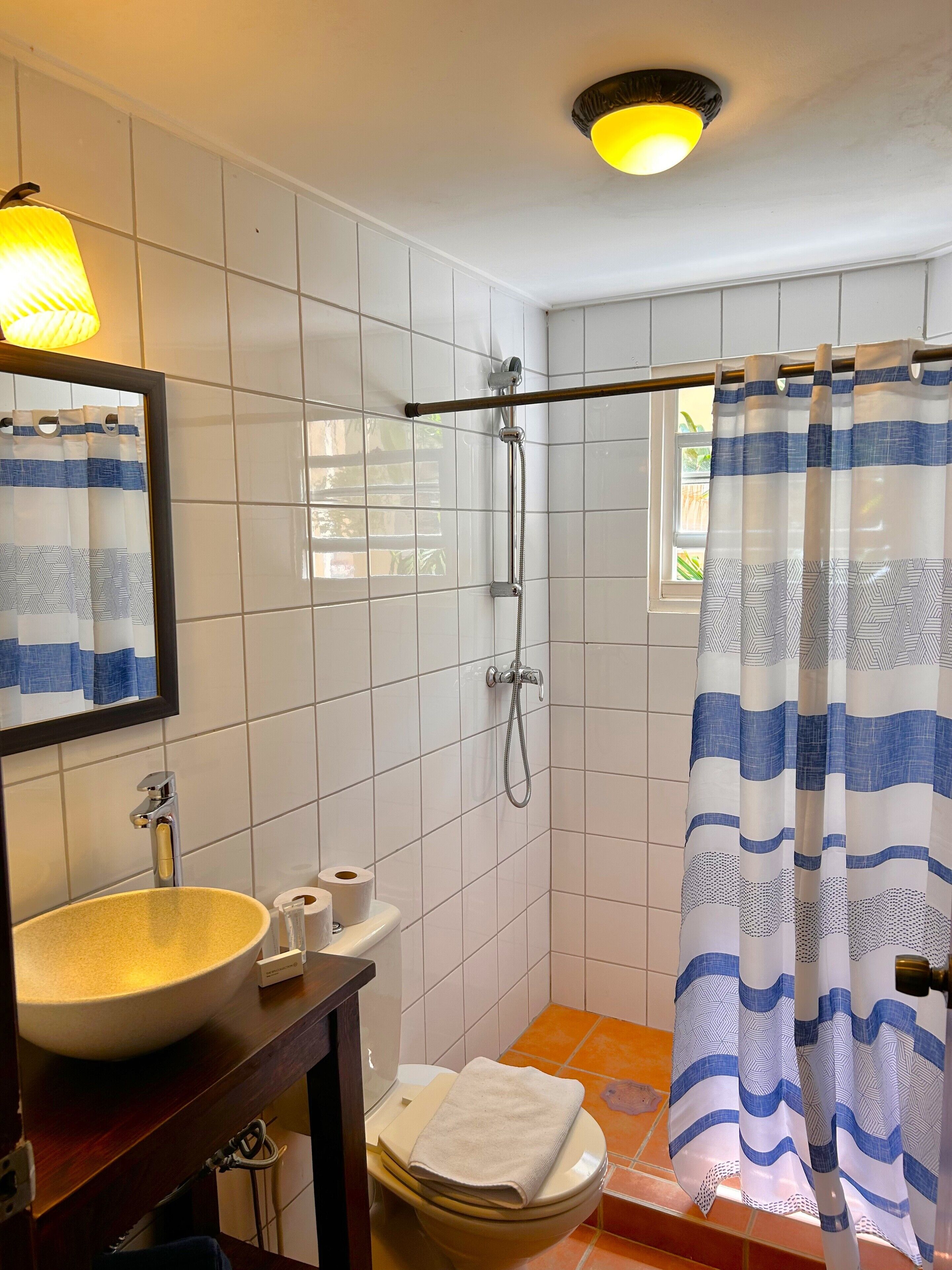 Un baño con inodoro, lavabo, ducha y una ventana con cortina.