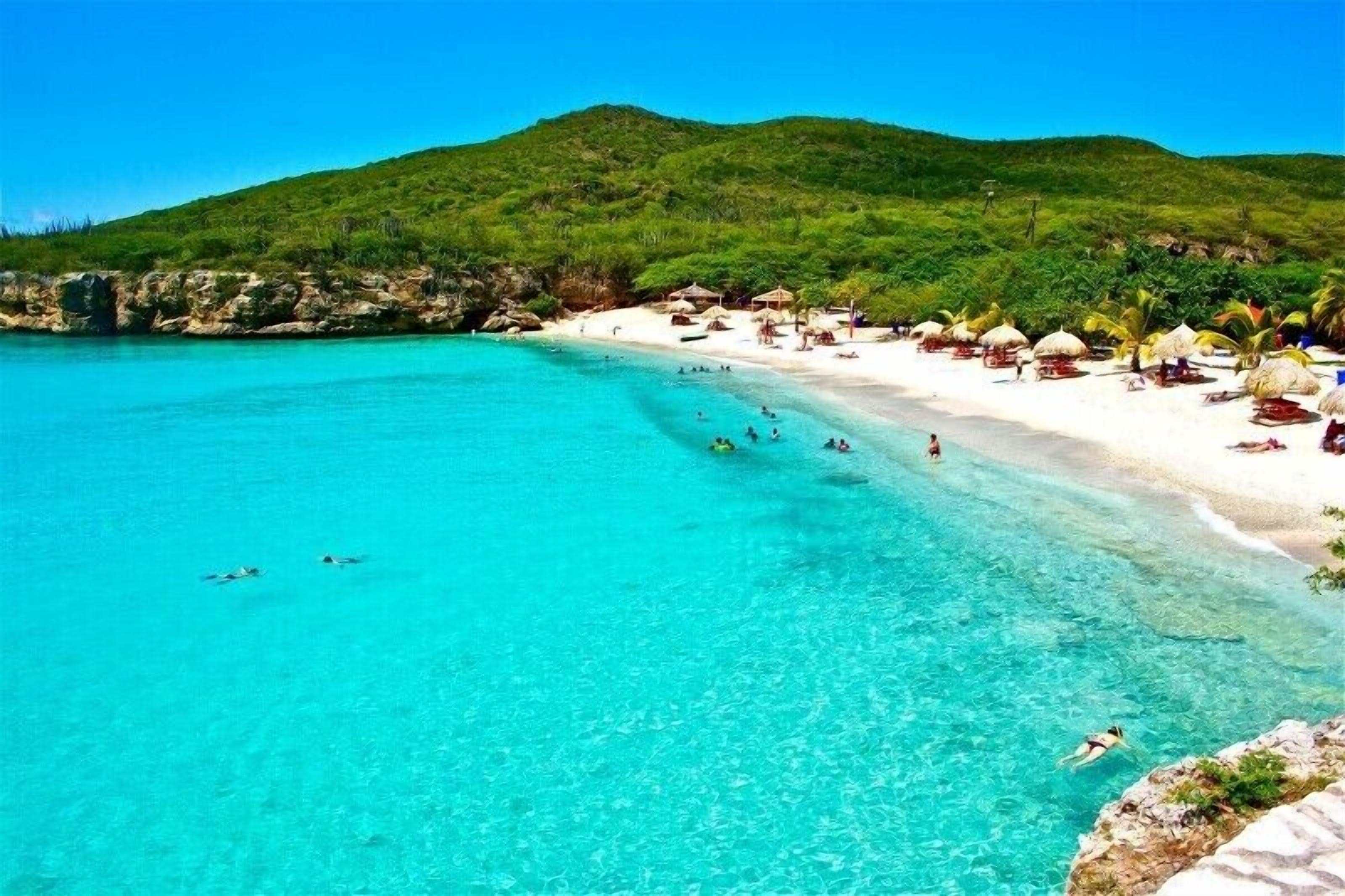 A beach with clear turquoise water, a sandy shore, and thatched-roof huts.