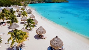 A beach with thatched umbrellas, palm trees, and sun loungers. - Lagun Blou Resort (Lagun)