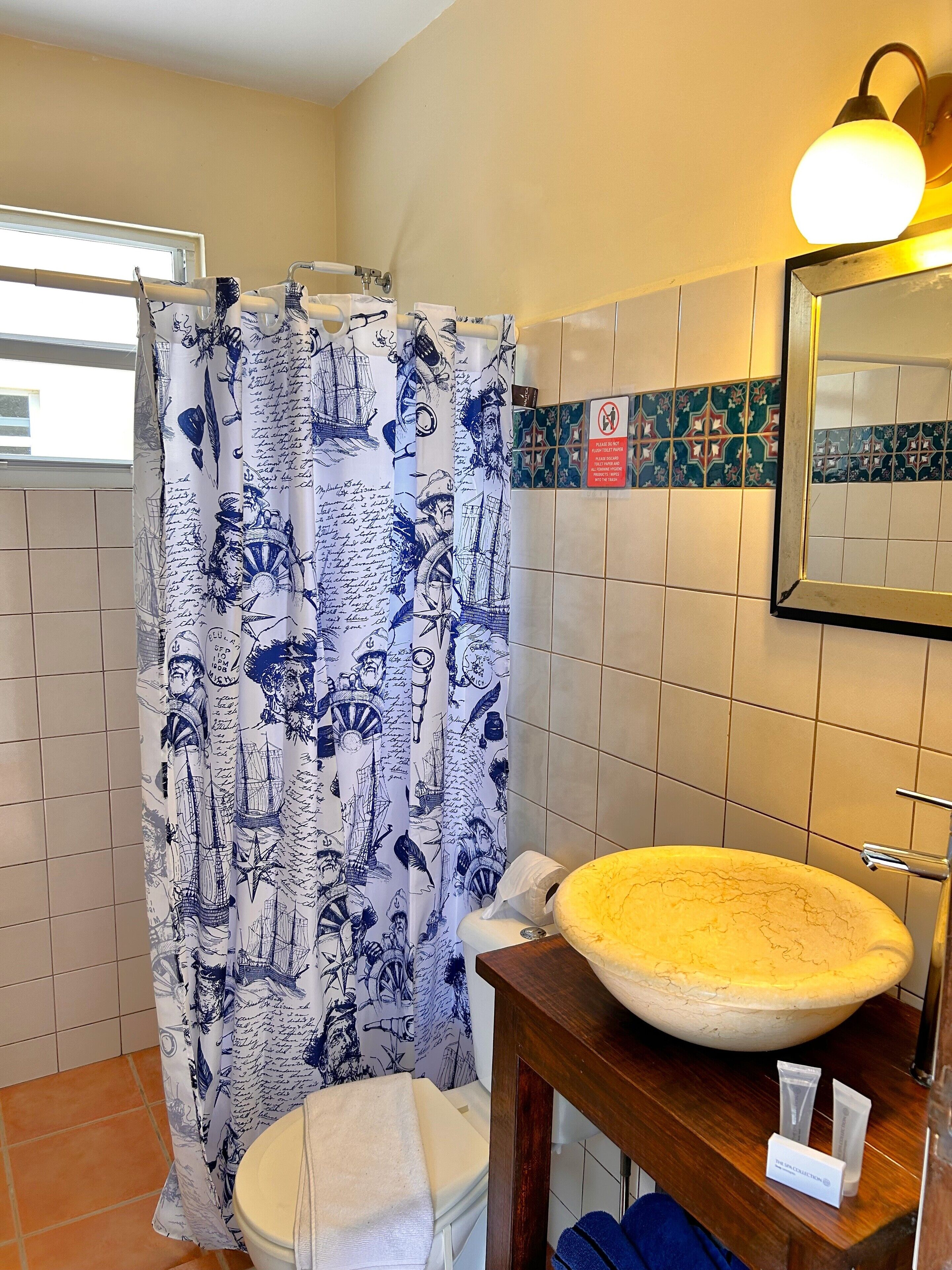 A bathroom with a large ship-themed shower curtain, a round sink with a basin, and a mirror above the sink.