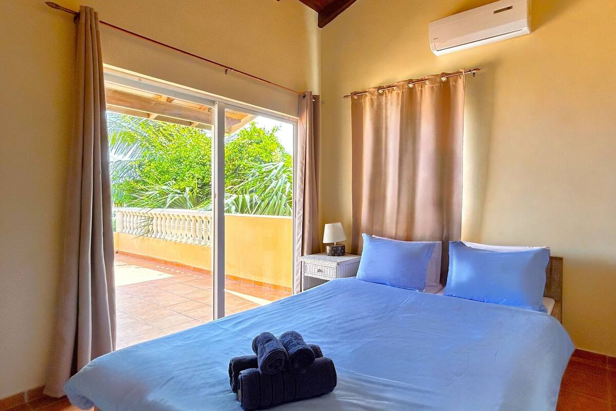 Habitación de hotel con cama, mesita de noche, lámpara y vistas al exterior.