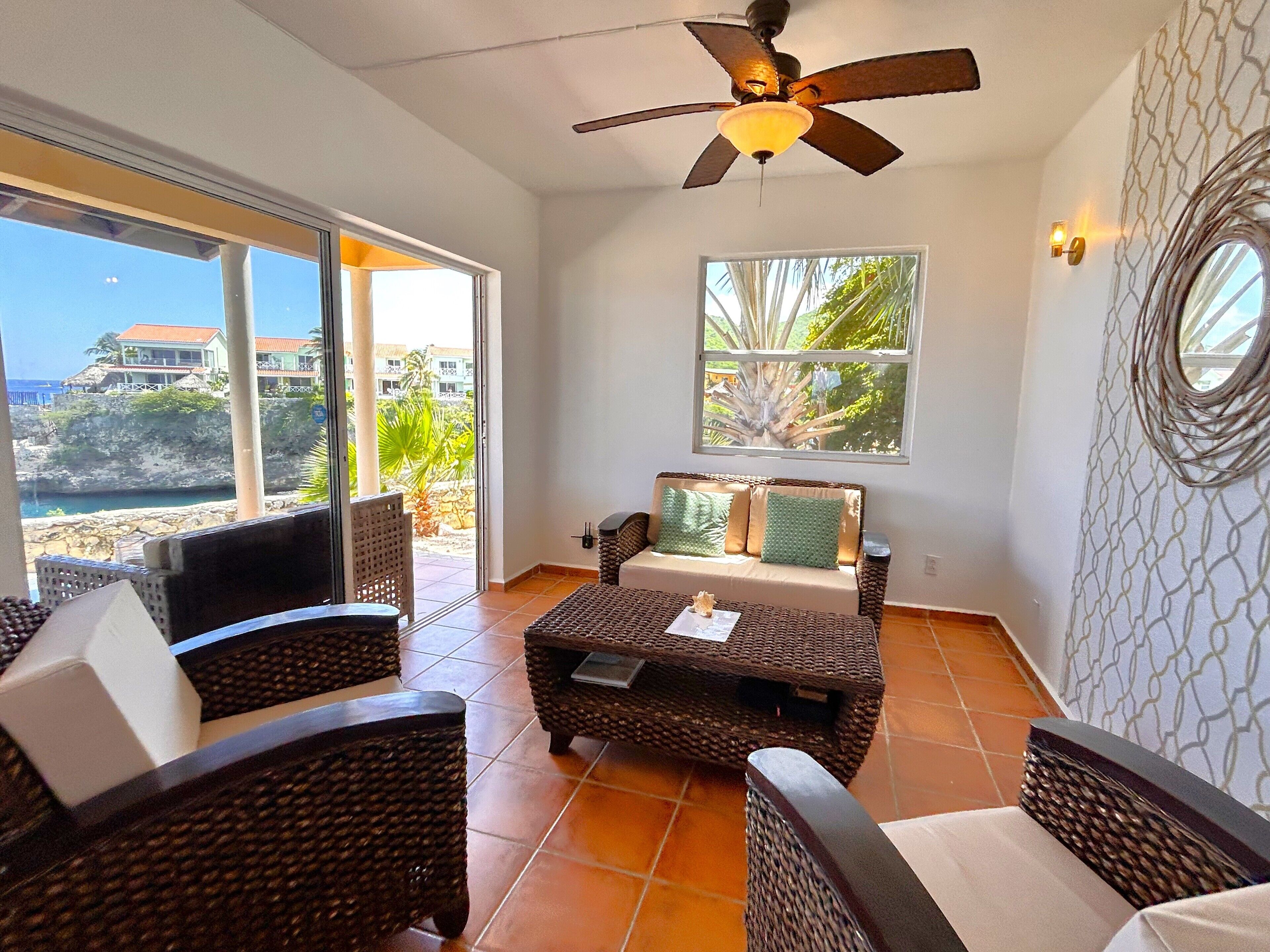 A room with wicker furniture, a ceiling fan, and a view of the ocean.