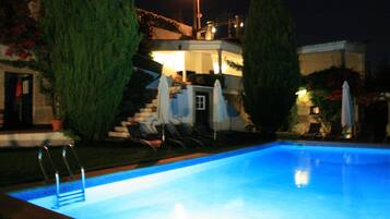 A swimming pool with a ladder, surrounded by lounge chairs and umbrellas, with a staircase leading to a building.