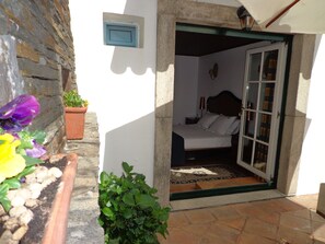 A small bedroom with a bed, a nightstand, and a window. There is a door leading to another room. - Casa de Canilhas (Mesão Frio)
