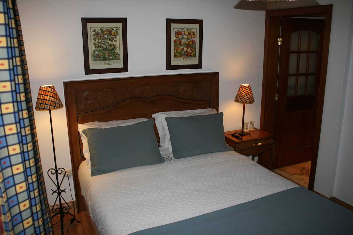 A neatly made bed with two pillows, a wooden headboard, and two wall-mounted lamps.