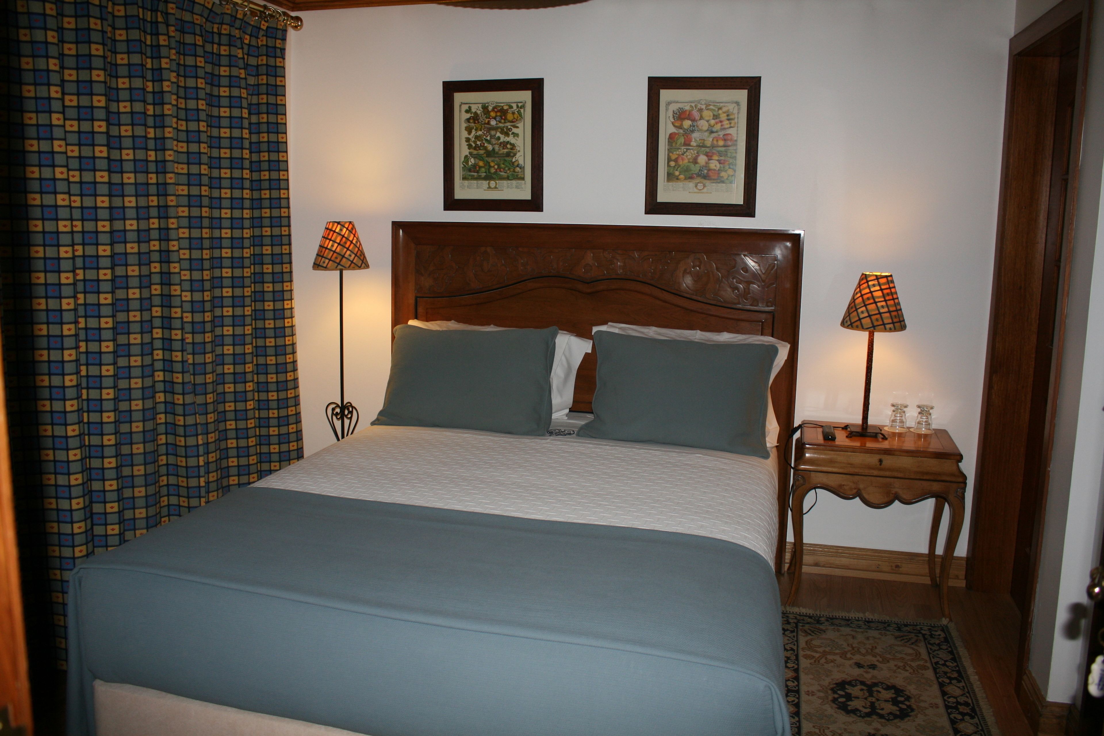 Una cama bien hecha con cabecera de madera, dos lámparas de noche y una cortina estampada.