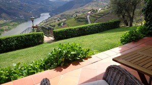 A patio with a wicker chair and a view of a river and mountains. - Casa de Canilhas (Mesão Frio)