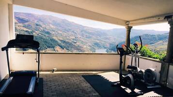 Un balcón con una caminadora y bicicletas estáticas, con vistas a un paisaje montañoso.