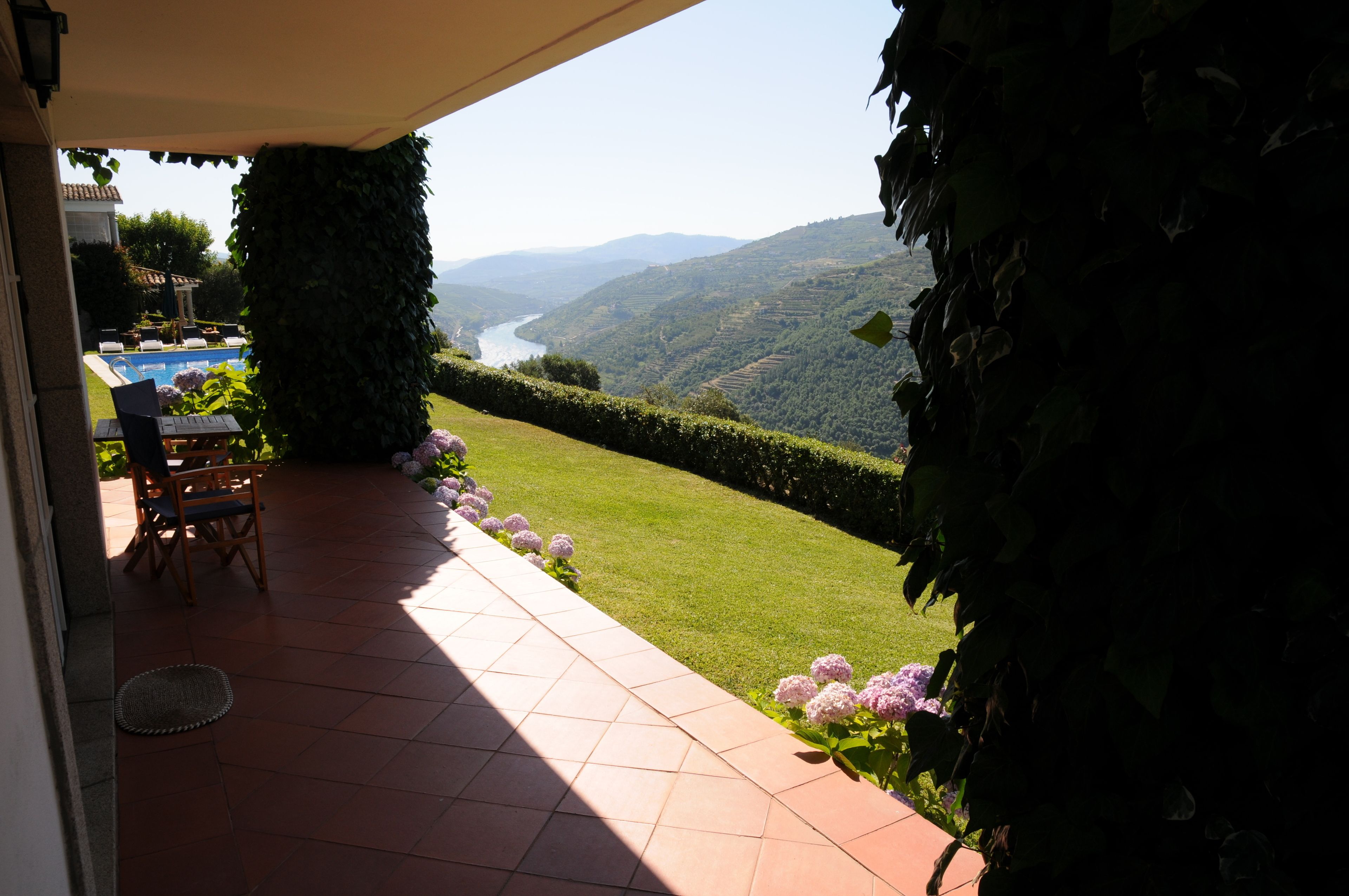 Eine Terrasse mit Blick auf einen Fluss und Hügel, ein überdachter Sitzbereich und ein gepflegter Rasen.