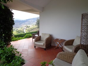 Una terraza con mobiliario de mimbre, una pequeña mesa y vistas a un paisaje montañoso.