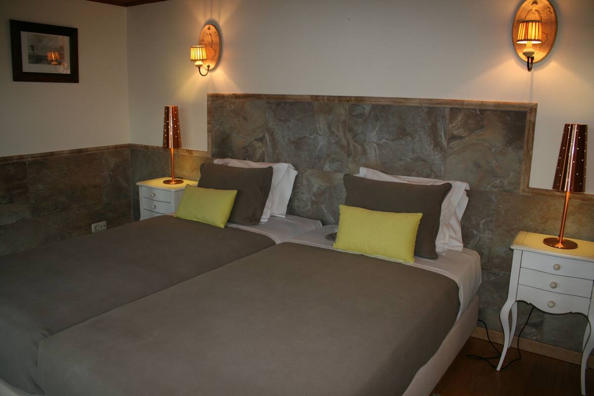 A double bed with a stone headboard, two bedside tables, and two wall-mounted lamps.