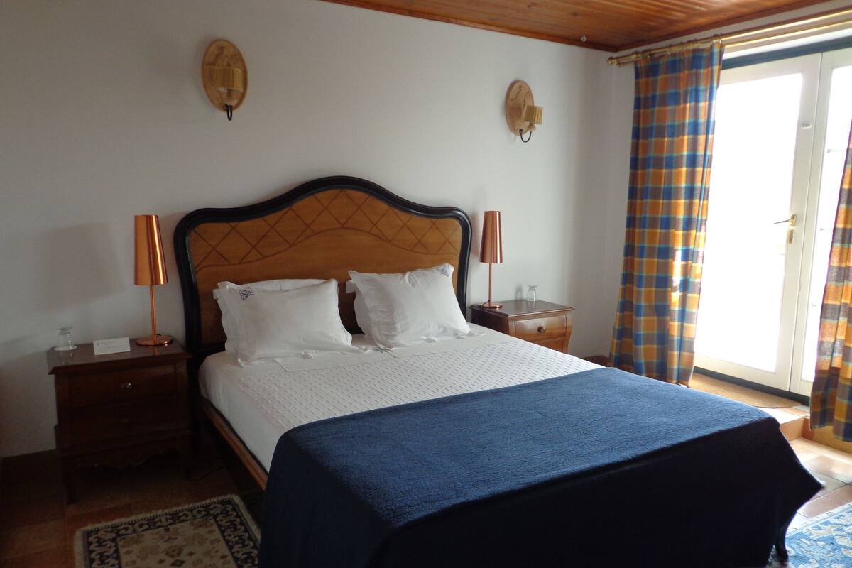A bedroom with a wooden headboard, two bedside lamps, a bed with white bedding, a blue throw, and a patterned rug.