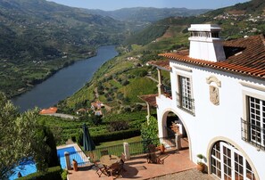 Un edificio blanco con tejado de baldosas que da a un río y colinas verdes exuberantes.