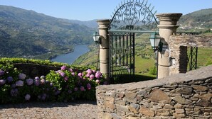 A stone gate with a metal decorative arch, leading to a scenic view of a valley and a lake. - Casa de Canilhas (Mesão Frio)