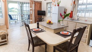 A modern kitchen with a dining area, a TV, and a balcony with a chair. - Bayside Villa St. Lucia (Castries)